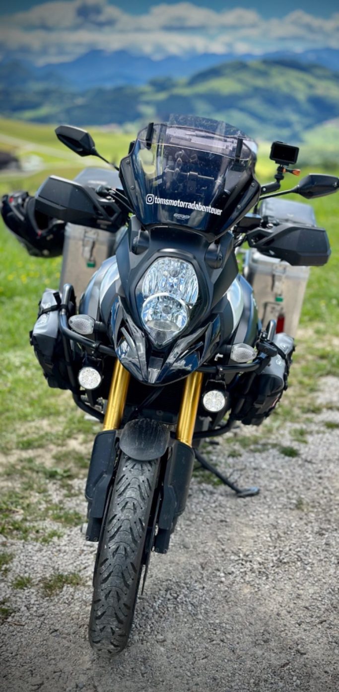 V-Strom in den Bergen Schwarze Suzuki V-Strom mit Gepäcktaschen, auf einem Feld mit Bergen im Hintergrund.