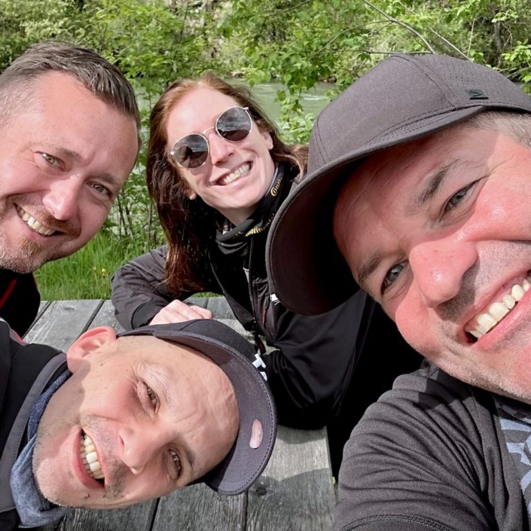 Biker Buddies Vier Personen lächeln in die Kamera, umgeben von grünem Hintergrund.