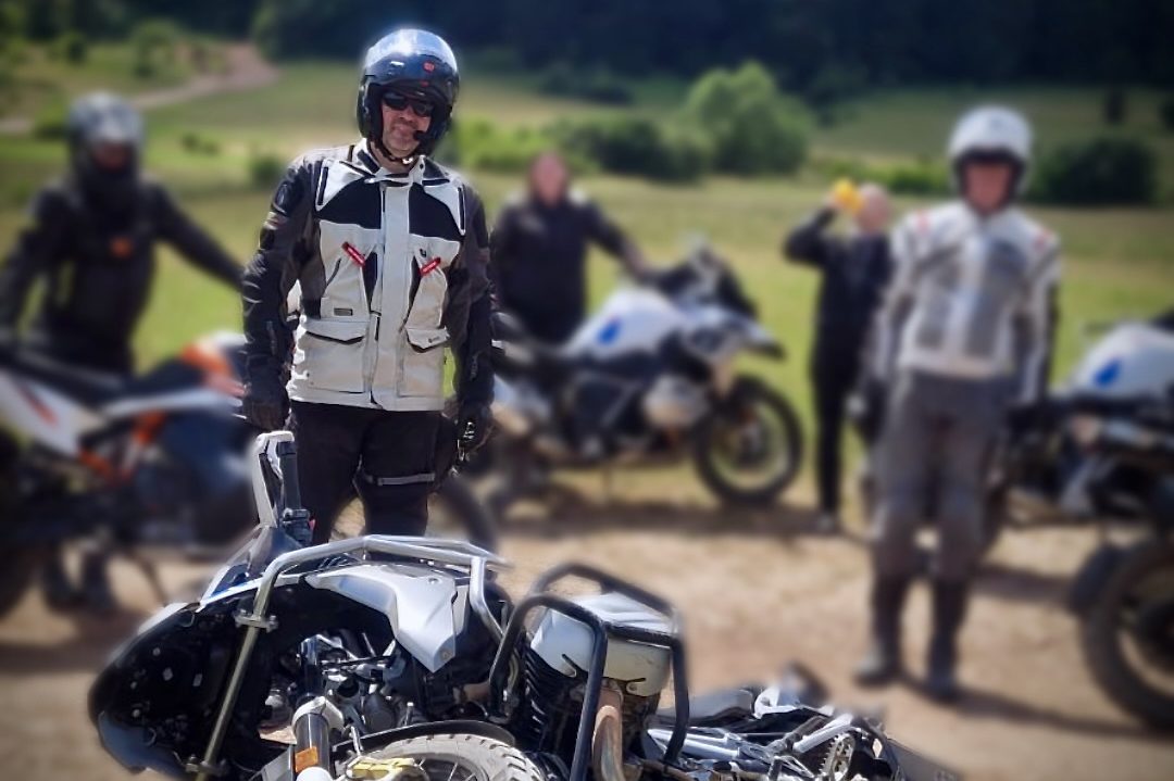 Crash beim Offroad Training Gruppe von Motorradfahrern auf einer grünen Wiese, einige stehen hinter einem umgefallenen Motorrad.